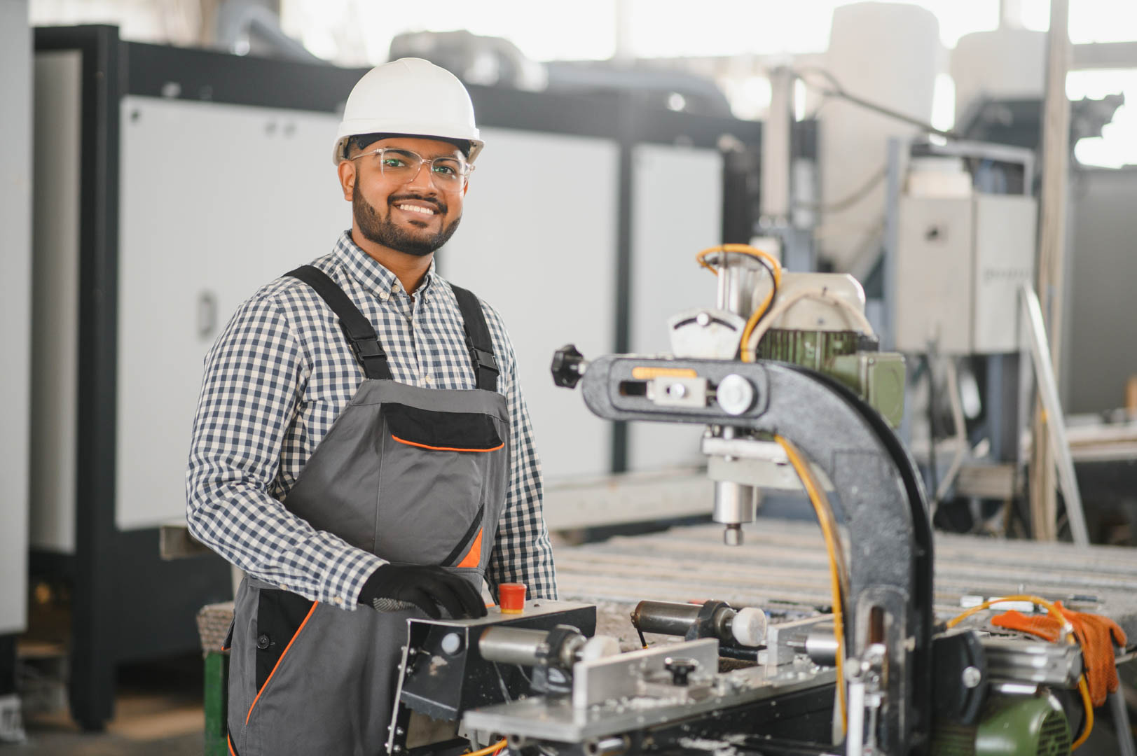 Operator of machine. Industrial worker indoors in factory. Young technician in white hard hat.